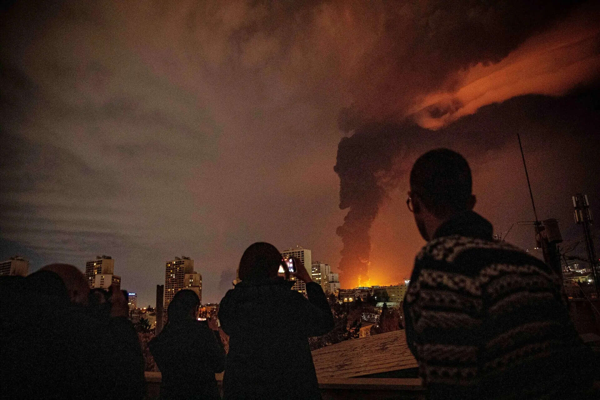 Residents look on and take pictures as flames and smoke rise from an oil storage facility struck as attacks hit the city during the U.S.–Israeli military campaign in Tehran, Iran, Saturday, March 7, 2026. (Alireza Sotakbar/ISNA via AP) Photos from Iran, Israel and Lebanon in the third week of the Iran war